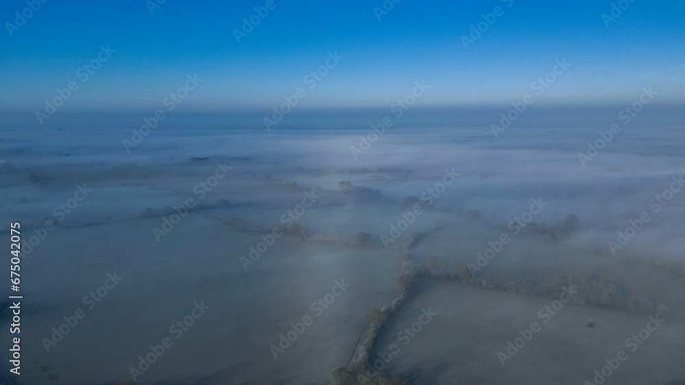 Aerial view of a small town shrouded in a misty fog, with white fluffy clouds surrounding it