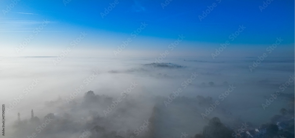 Aerial view of a small town shrouded in a misty fog, with white fluffy clouds surrounding it