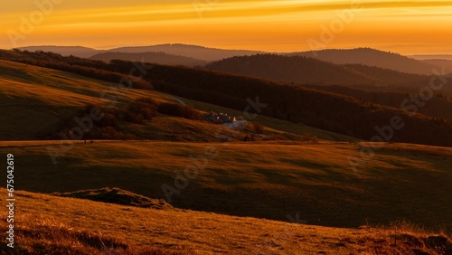 Idyllic countryside scene of rolling hills with yellow grass silhouetted against the setting sun