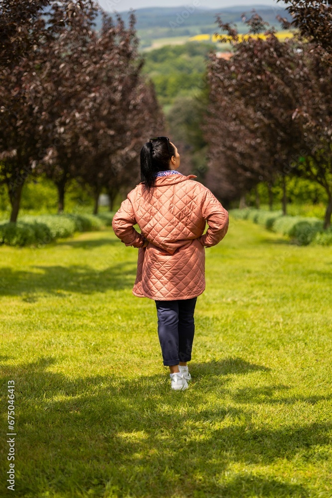 Vertical of a female in a coat, walking on green grass in a park