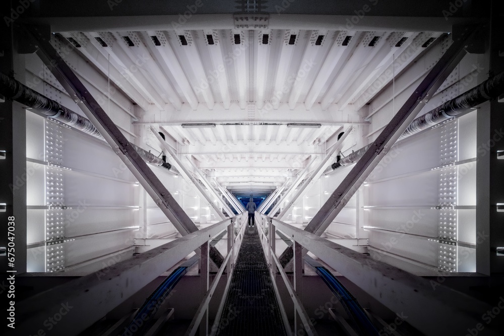 Obraz premium Person standing inside a symmetrical man-made interior walkway with multiple levels and floors