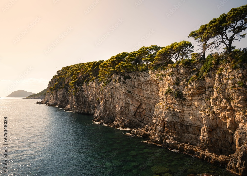 Birds eye view of a coastal cliff covered with grass and trees during a beautiful sunset