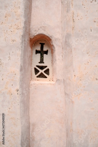 Vertical shot of a window carved on a pink wall in the shape of a cross