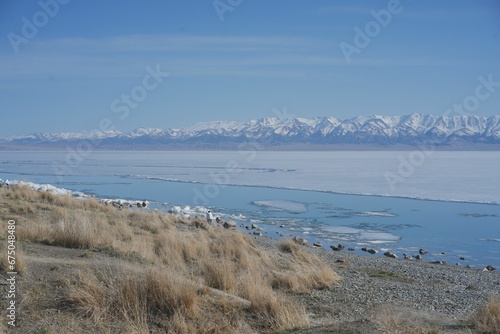 Scenic view of a frozen shore against a lake and a snowy mountain range in winter