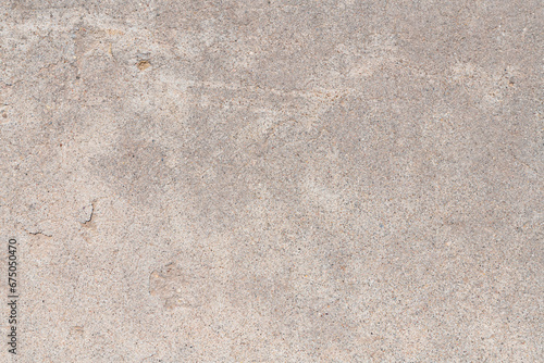 Detail of a section of weathered concrete sidewalk with a rough texture, gray colors, and thin cracks and chips in the surface.