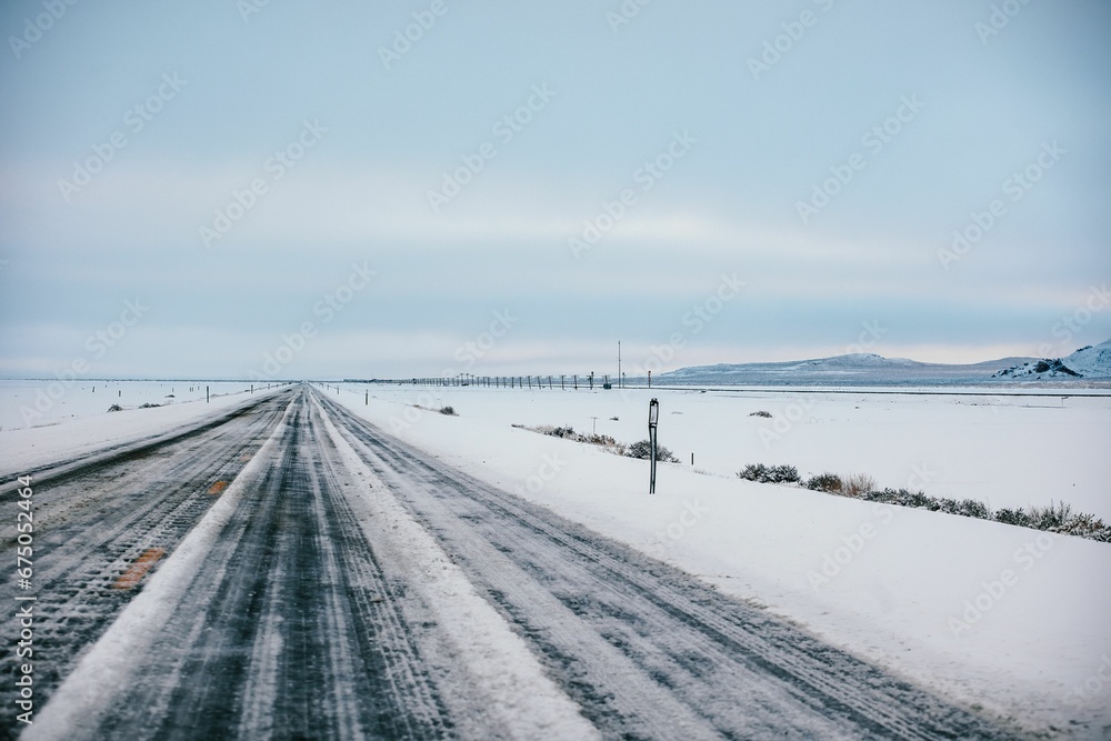 a lone road running through the snow covered ground below a cloudy sky