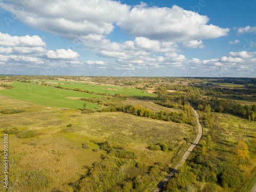 Aerial view of the cloudy blue sky over the idyllic rural landscape featuring a winding road