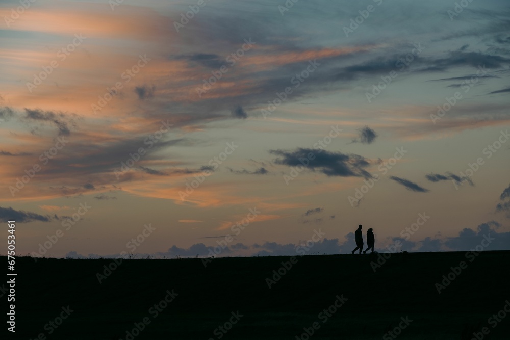 two people walk across a field while the sky is cloudy