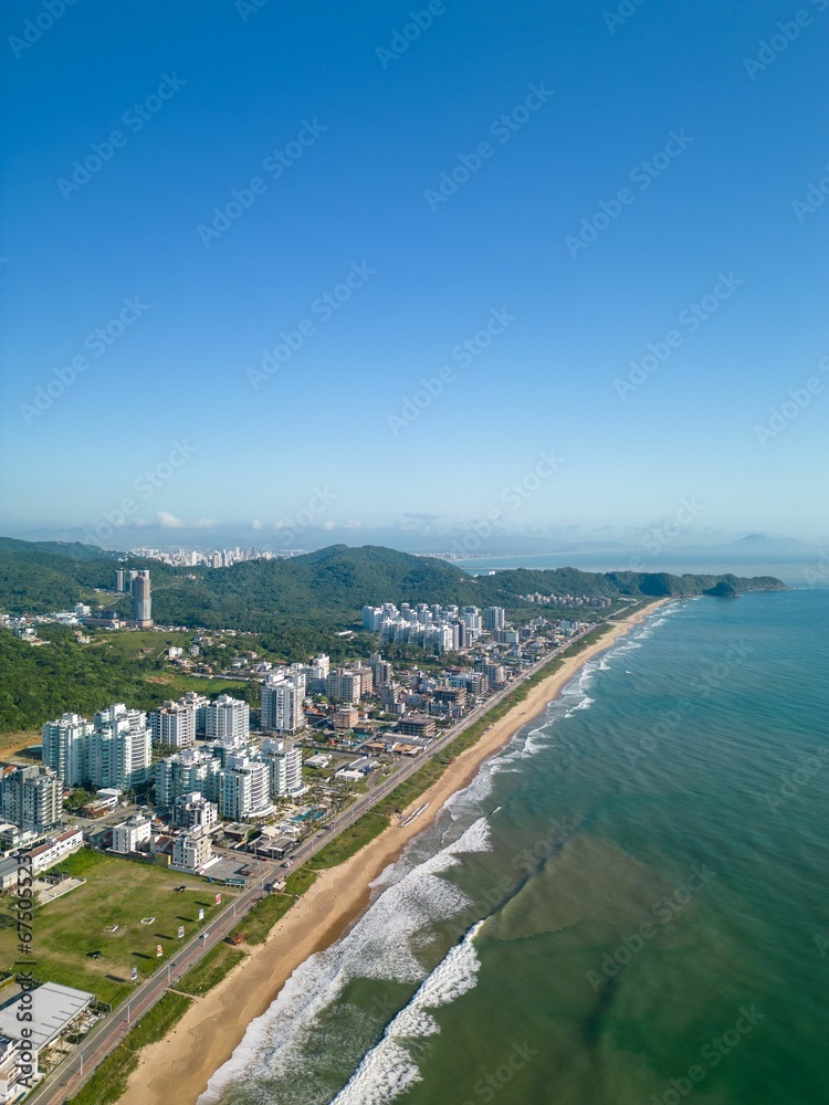 Fototapeta premium Aerial view of a beach and Praia Brava cityscape in the background under the blue sky
