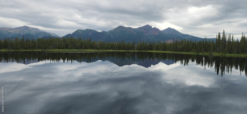 Panoramic view of green trees and mountains reflecting on a tranquil lake on a cloudy day