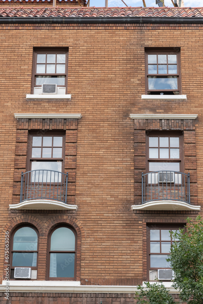 Facade of a vintage looking brick apartment building with windows and air conditioning units visible.
