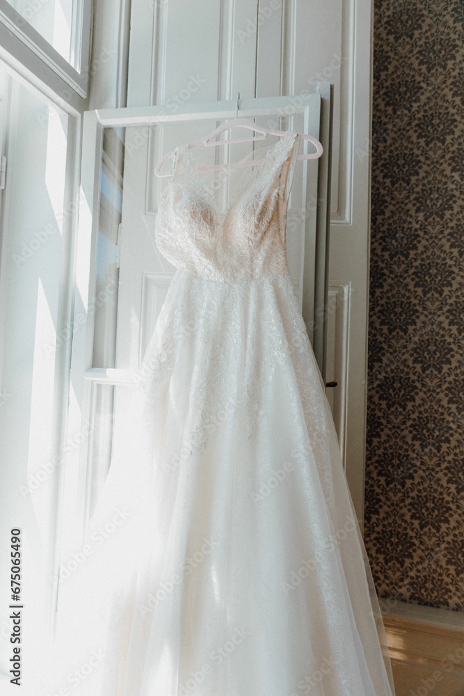 Closeup shot of a stunning white bridal dress hanging in a well-lit room Closeup shot of a stunning white bridal dress hanging in a well-lit room