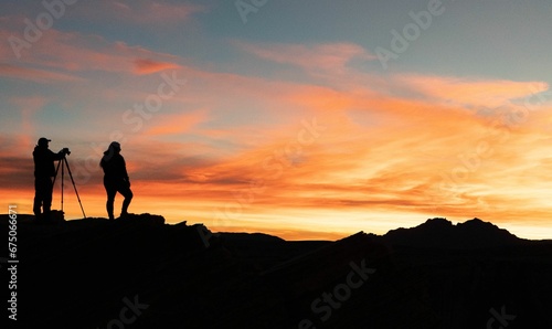 Silhouetted individuals are capturing the stunning sunset with their camera equipment © Wirestock