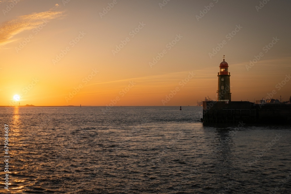 Picturesque lighthouse illuminated by the setting sun, which casts a few clouds in the sky
