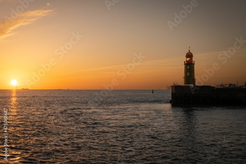 Picturesque lighthouse illuminated by the setting sun, which casts a few clouds in the sky