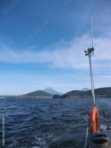 Leaving the harbor on sailing yacht, Kamchatka mountains, distant Koryaksky and Avachinsky volcanoes  in background behind the ship stern photo