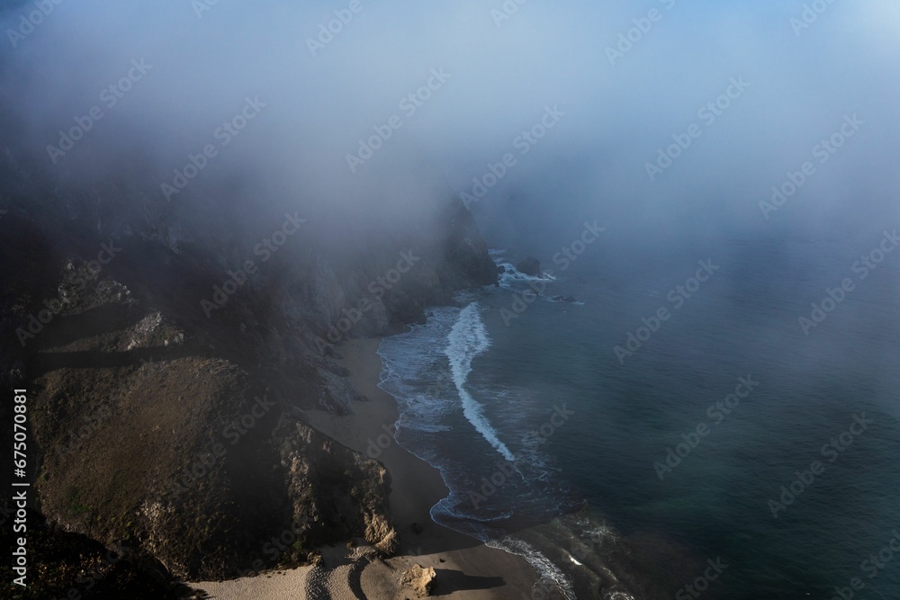 Stunning landscape of a beach surrounded by majestic mountains covered in fog