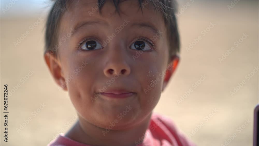 Close up of a funny young expressive latin hispanic boy with grains of sand on his cheeks talking to the camera in slow motion Close up of a funny young expressive latin hispanic boy with grains of sand on his cheeks talking to the camera in slow motion
