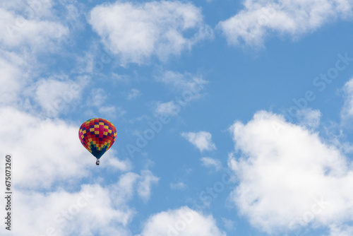 An isolated multicolored hot air balloon floats in the air with white clouds and a crisp blue sky.