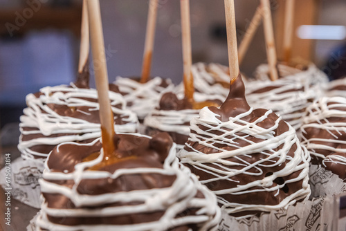 Several chocolate dipped caramel apples with a white chocolate drizzle arranged in a display at a market during the winter holidays. photo