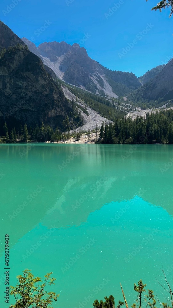 a mountain range over a large blue-green lake with trees around it: Lago di Braies