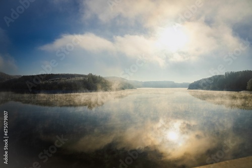 Tranquil scene of a lake surrounded by trees  with a blanket of mist obscuring the ground