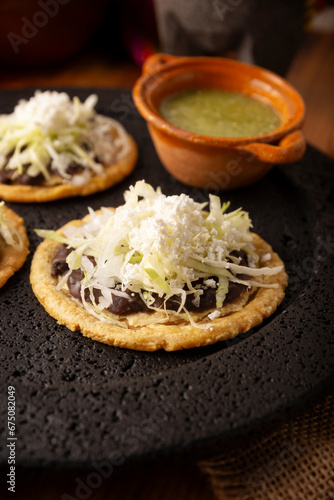 Sopes. Mexican typical food prepared with flattened fried corn dough covered with refried beans, green or red sauce, lettuce, cheese, onion and sour cream. Served on stone comal plate.