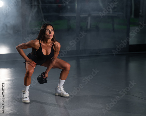 A beautiful brunette with big breasts does Russian swings with a kettlebell.