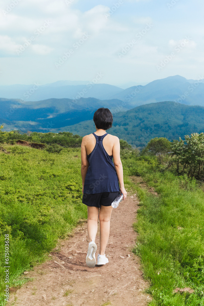 Woman exercise walking on hillside trail with mountain view.