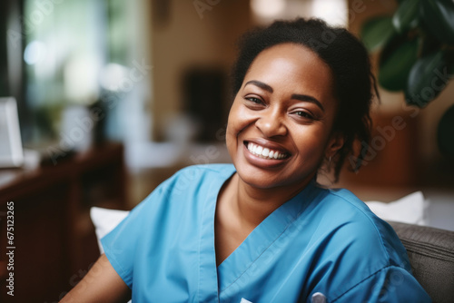 Smiling woman wearing blue scrub suit is seated comfortably on couch. This image can be used to depict healthcare professional or medical worker in relaxed setting.