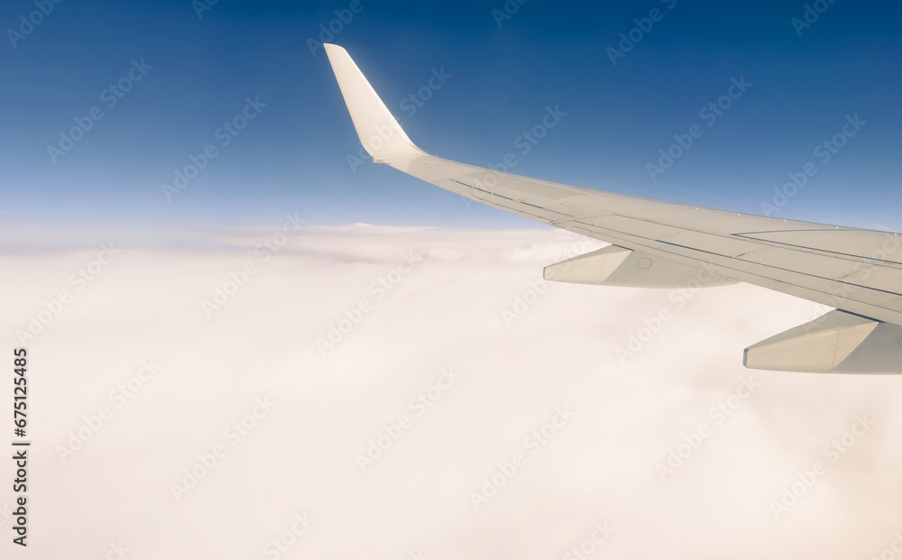 Obraz premium White wing from airplane window on sunny day. Great views of landscape. Aerial view of clouds through a plane window. Wing of airplane with blue sky and beauty clouds