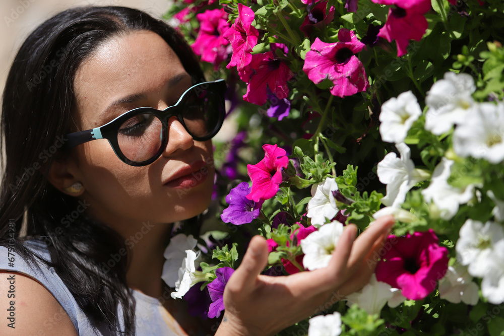 Portrait of a young, beautiful, dark and South American woman with a printed shirt and sunglasses, smelling flowers of different colors that she holds with her hand. Concept beauty, flowers, spring. Portrait of a young, beautiful, dark and South American woman with a printed shirt and sunglasses, smelling flowers of different colors that she holds with her hand. Concept beauty, flowers, spring.