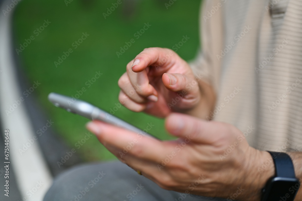Cropped shot of middle age man using mobile phone while sitting in the public park