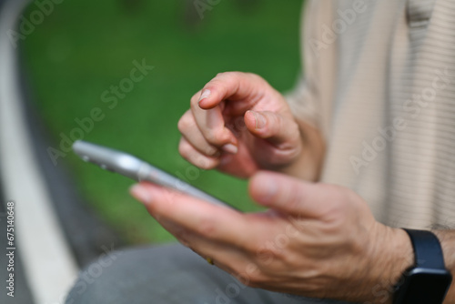 Cropped shot of middle age man using mobile phone while sitting in the public park