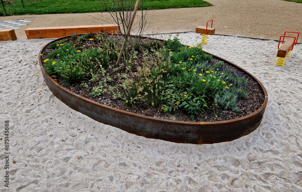 the oval ellipse of the flower bed is lined with a rusty sheet metal border. perennials are blooming. sandpit with park features and children's playground. rounded edge, stepping stones, concrete the oval ellipse of the flower bed is lined with a rusty sheet metal border. perennials are blooming. sandpit with park features and children's playground. rounded edge, stepping stones, concrete
