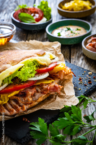 Big sandwich with grilled chicken breast and cheese and fresh vegetables on wooden table

