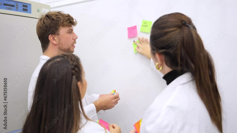 Group of young scientists having brainstorming. Chemists sticking adhesive notes on board. Group of young scientists having brainstorming. Chemists sticking adhesive notes on board.