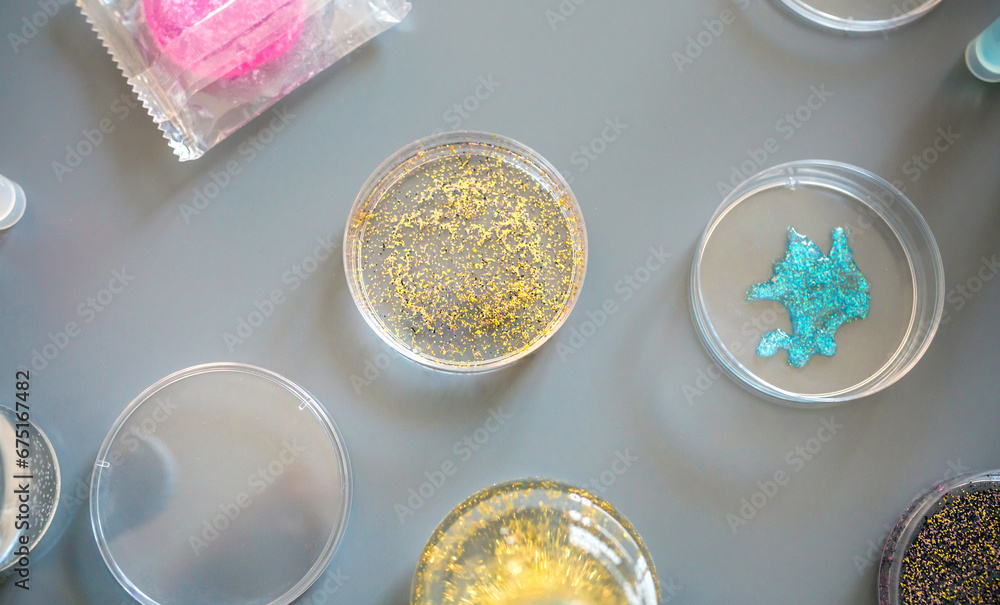 Top view of different glitter samples in petri dishes over a lab table background. Small plastic particles behavior to humans and environment. Concept of European Union ban use of microplastics. Top view of different glitter samples in petri dishes over a lab table background. Small plastic particles behavior to humans and environment. Concept of European Union ban use of microplastics.