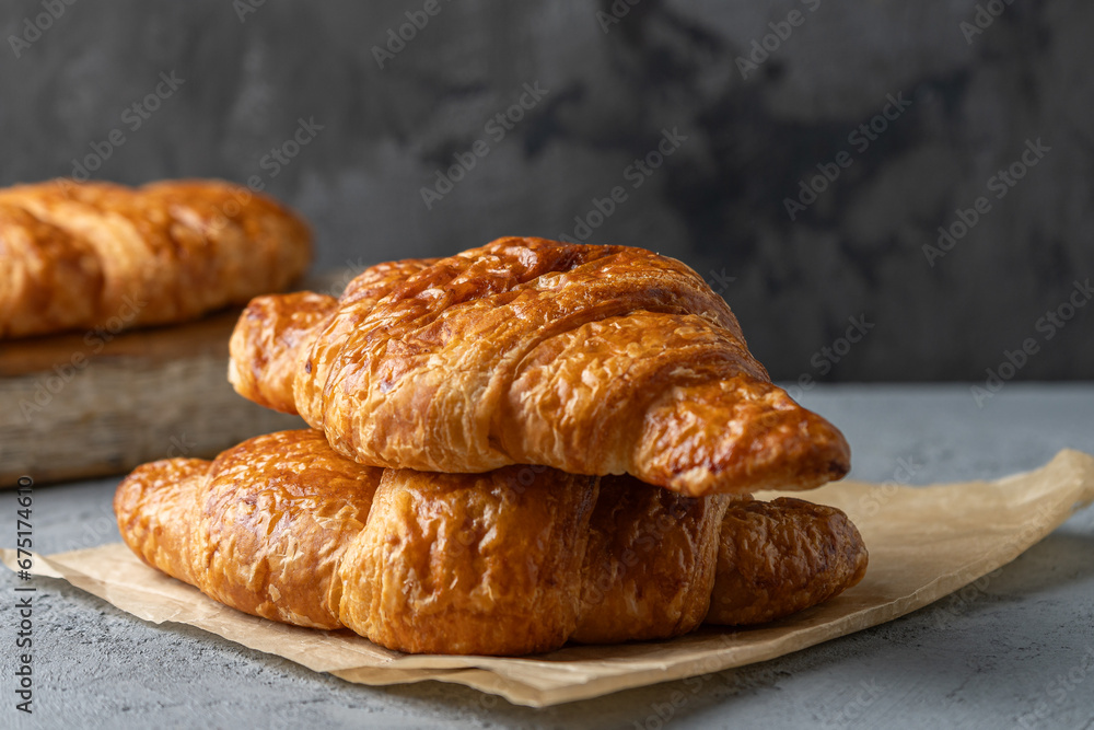 Fresh croissants with a golden brown and crispy crust on baking paper and against the background of an old dark concrete wall.