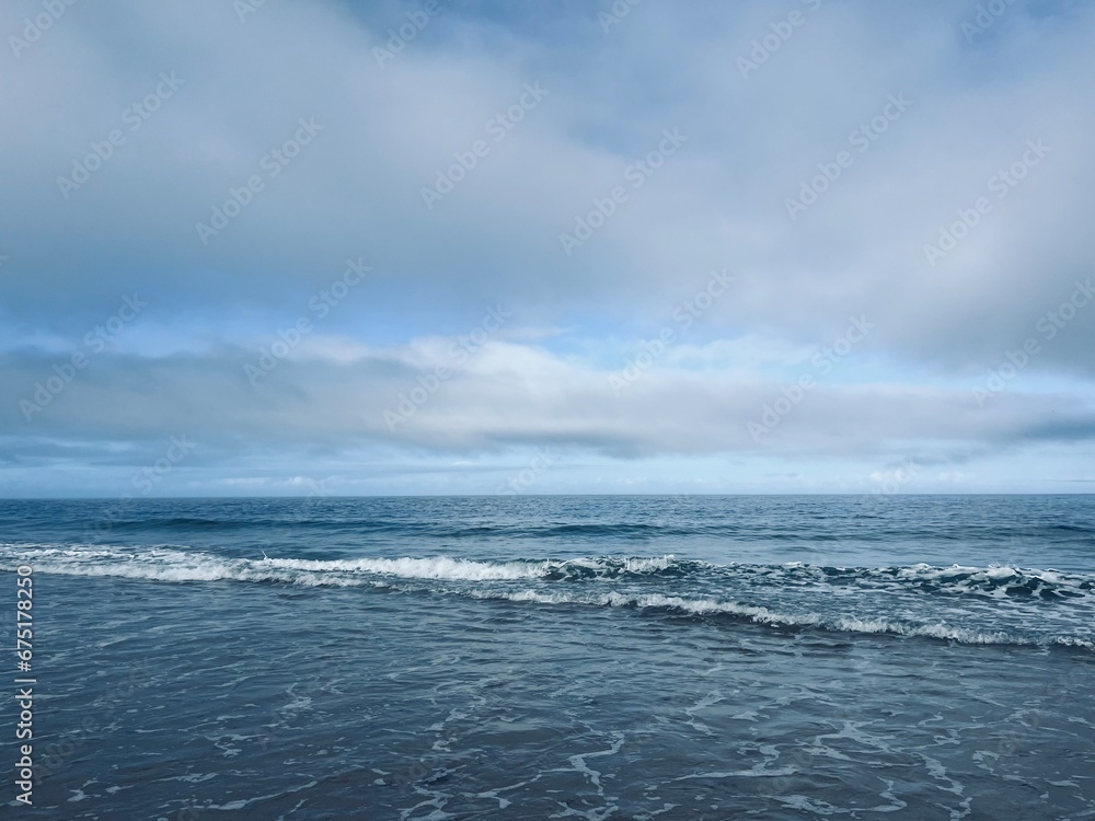 Waved ocean horizon, ocean coastline, sandy shore, splash and foam, cloudy sky, windy
