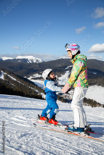 preschool boy and teenage girl stand on a mountain slope on skis holding hands. Ski lessons for children. Winter sports for the family. Frosty sunny weather. helping younger brother from older sister