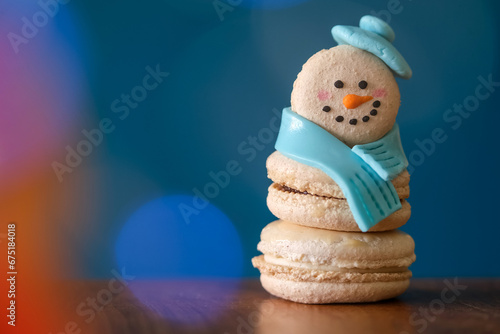 Snowman macaron dessert decorated with hat and scarf against colorful lights and bokeh background. Merry Christmas and Happy New Year festive concept photo