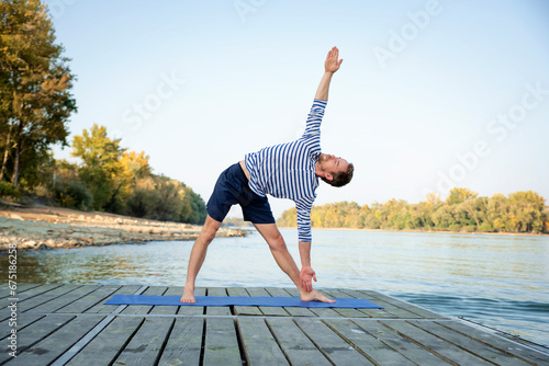 Active man practicing yoga on the pier by the river