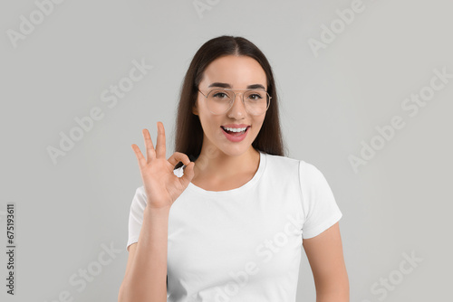 Wallpaper Mural Beautiful woman in glasses showing OK gesture on light gray background Torontodigital.ca