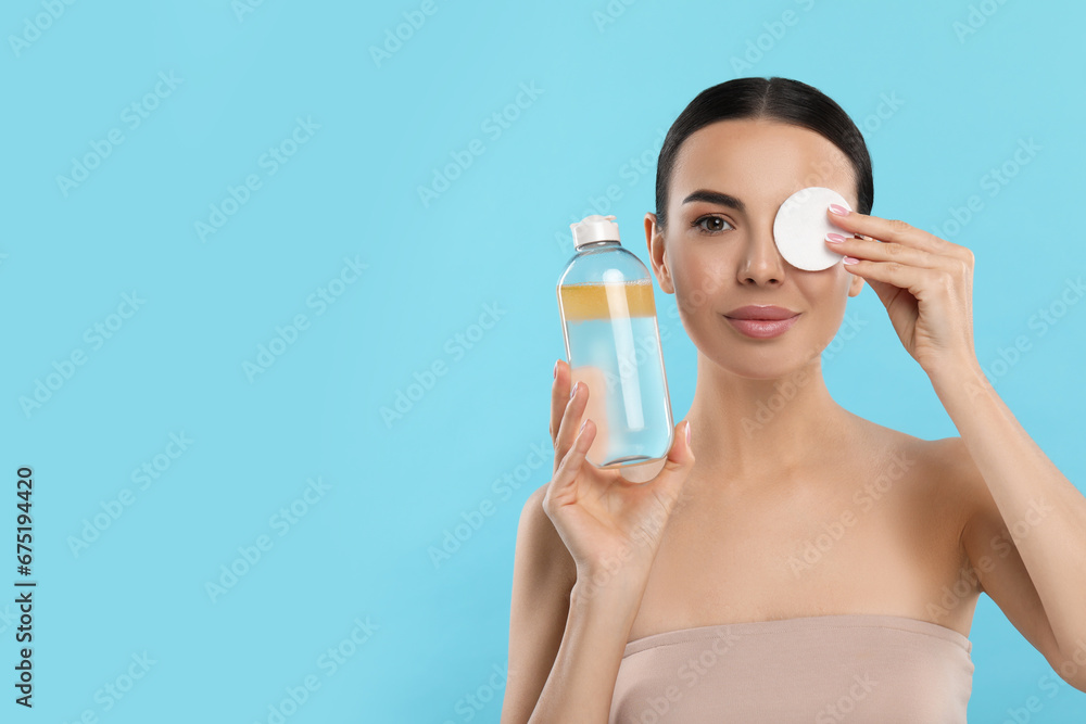 Beautiful woman removing makeup with cotton pad on light blue background, space for text Beautiful woman removing makeup with cotton pad on light blue background, space for text