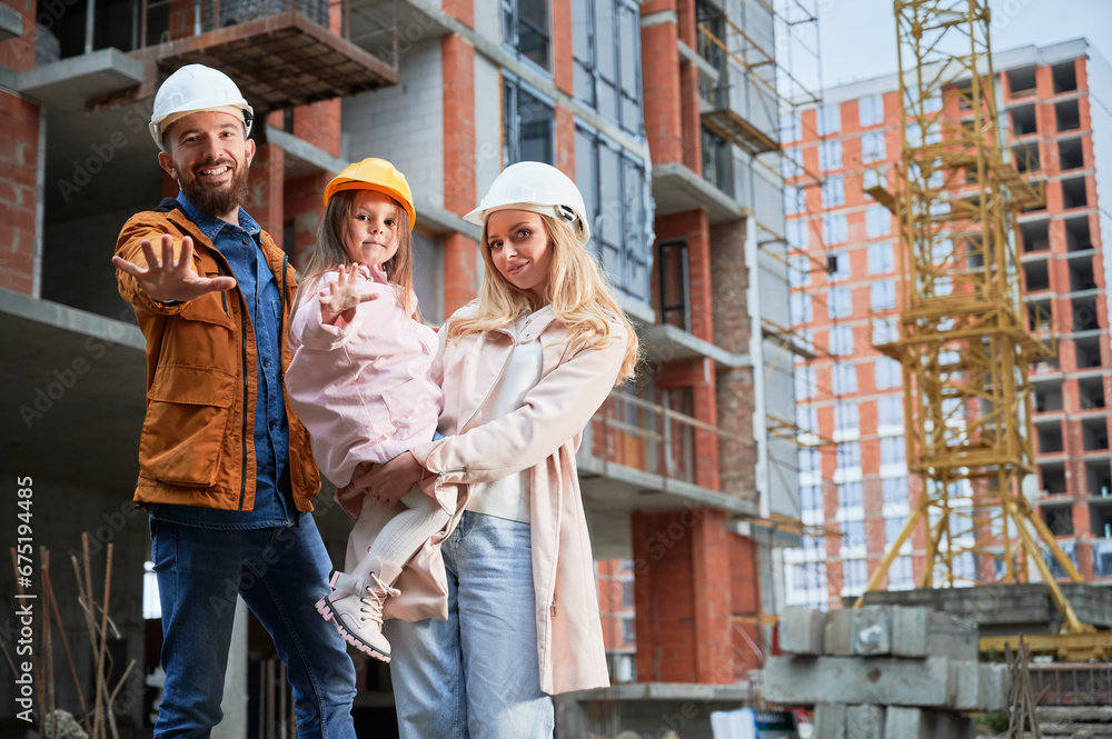 Man, woman and child standing outside building under construction. Happy family homeowners posing on the street at construction site. Man, woman and child standing outside building under construction. Happy family homeowners posing on the street at construction site.