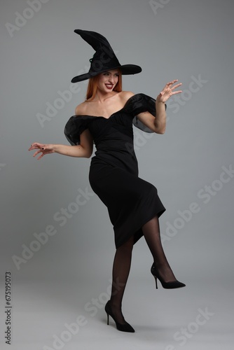 Happy young woman in scary witch costume posing on light grey background. Halloween celebration