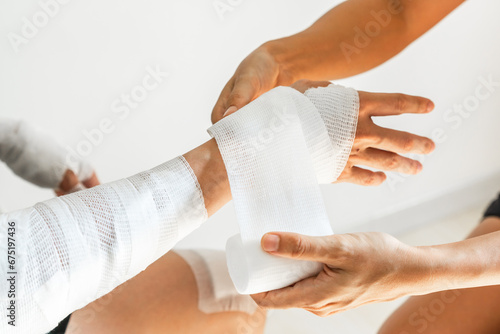Sister wrapping her brother wrist and arm with bandage around injured hand over white background at home. First aid, accident and injury treatment concept. Closeup photo