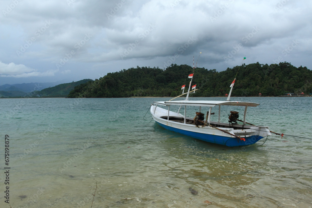 Empty wooden boat with small Indonesian flags on top moorer on seaside.