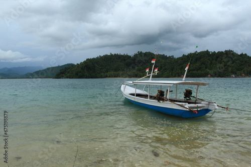 Empty wooden boat with small Indonesian flags on top moorer on seaside.
